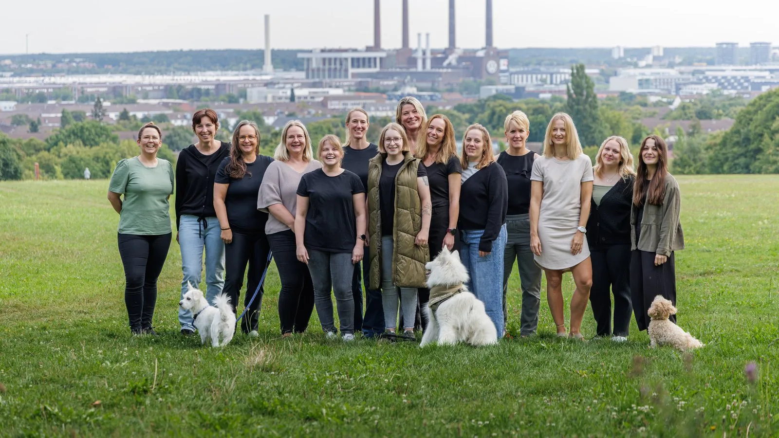 Das Team der Praxis ErgoLogo in Wolfsburg mit den drei Therapiebegleithunden vor der Stadtkulisse
