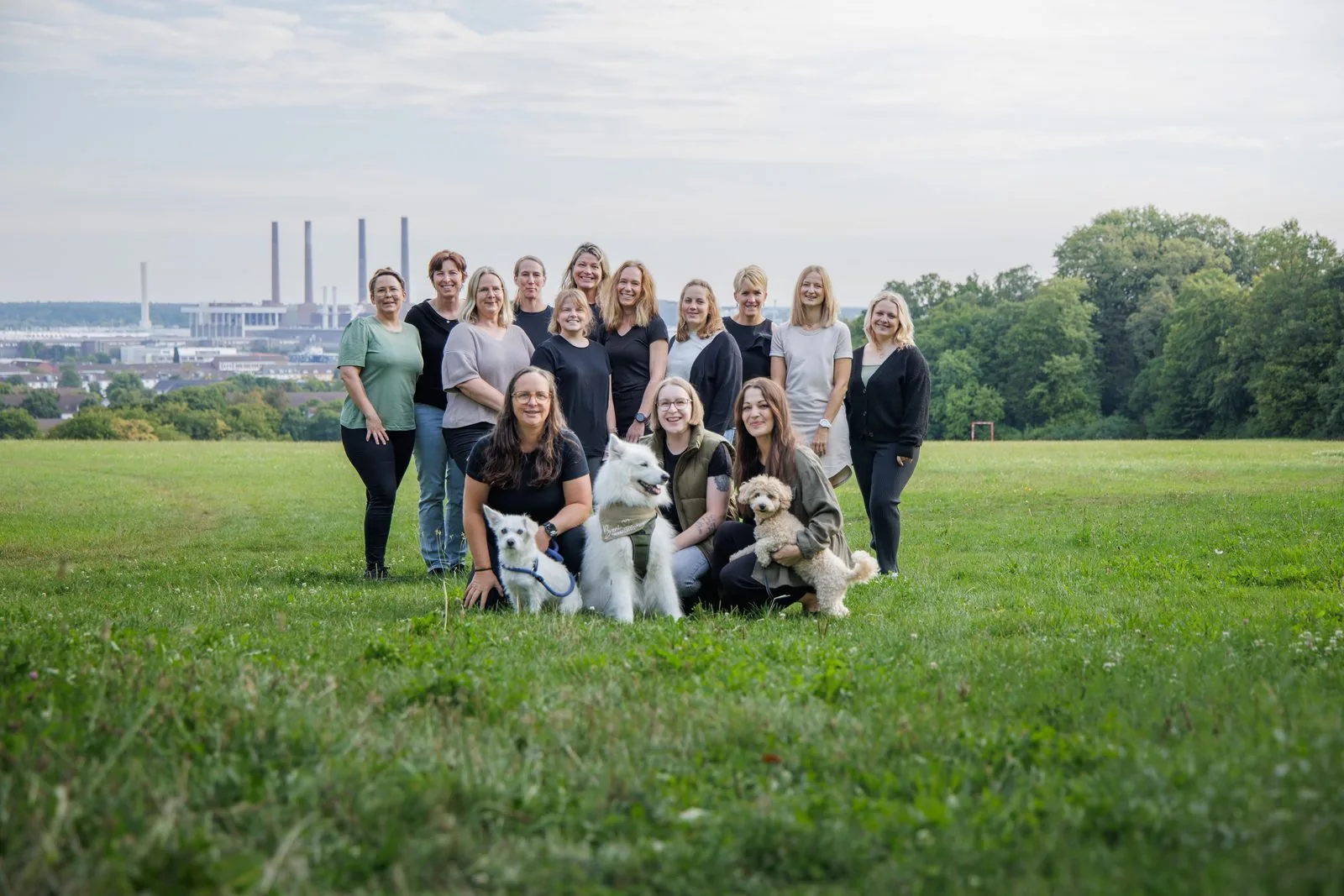 Das gesamte Team der Praxis ErgoLogo mit den drei Therapiebegleithunden vor der Kulisse Wolfsburgs